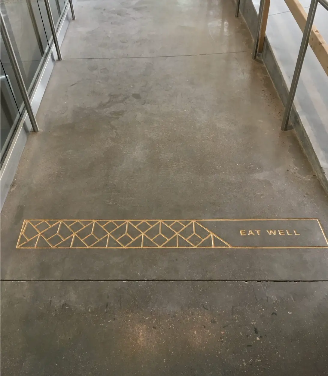 Eat Well truss graphic engraved in gold on a concrete walkway